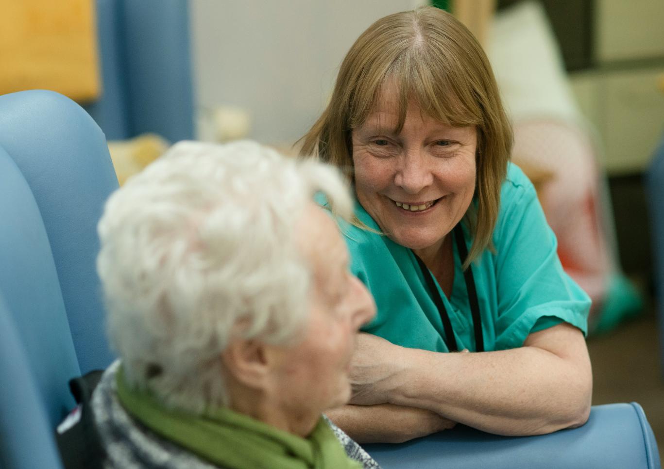 Nurse in turquoise uniform smiling at elderly woman