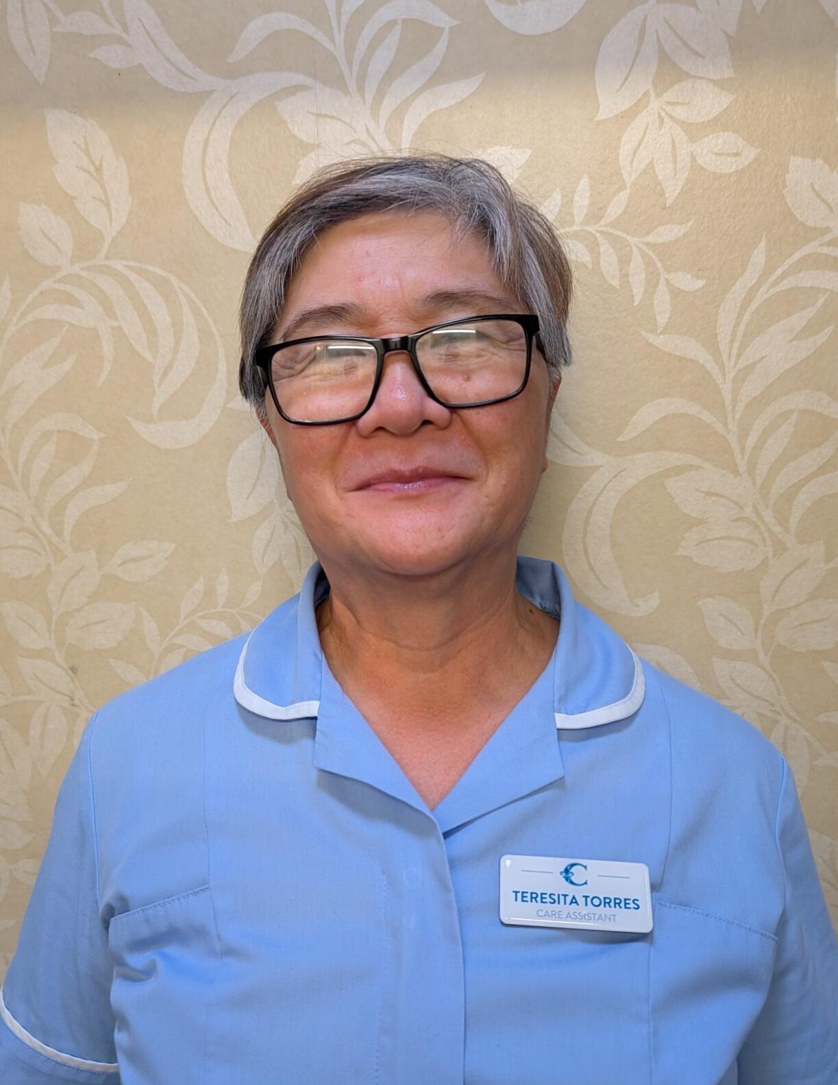 woman with glasses in blue nurses uniform smiling