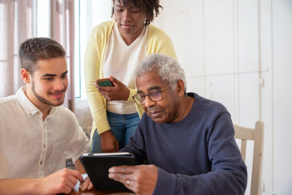 Man helping an elderly couple research care homes on a tablet