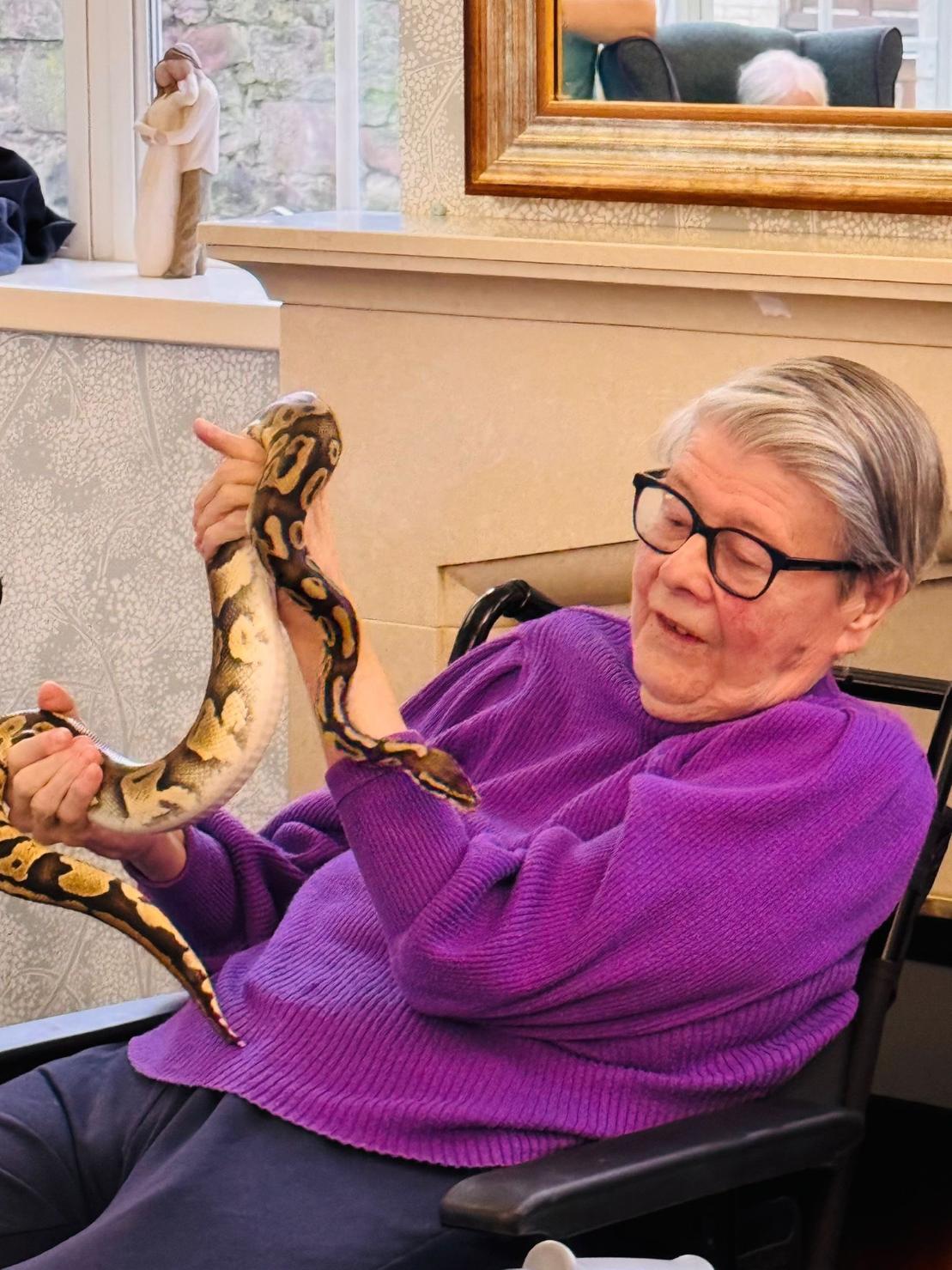 elderly woman in purple jumper holding a snake