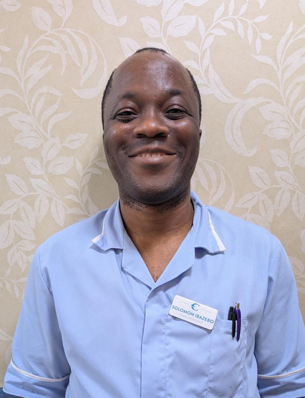 a man smiling in a light blue nurses uniform