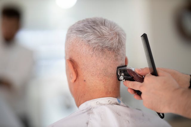 barber using hair clippers on elderly man
